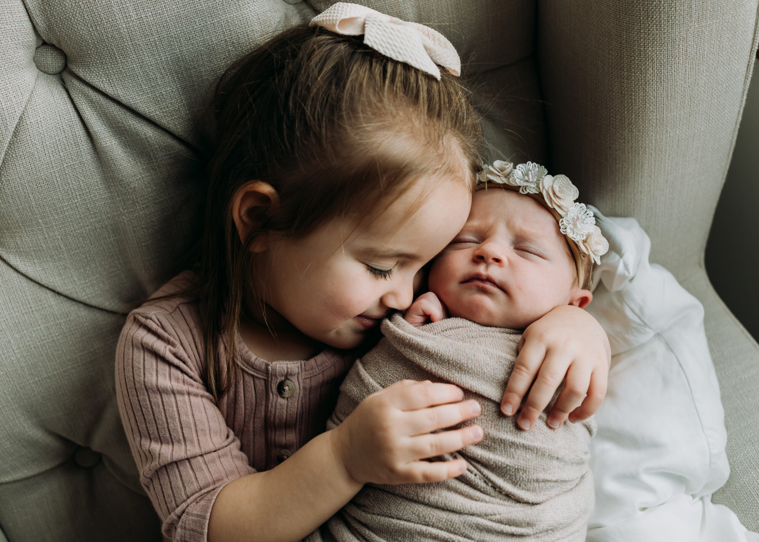 Toddler holding her baby sister for newborn photos at home