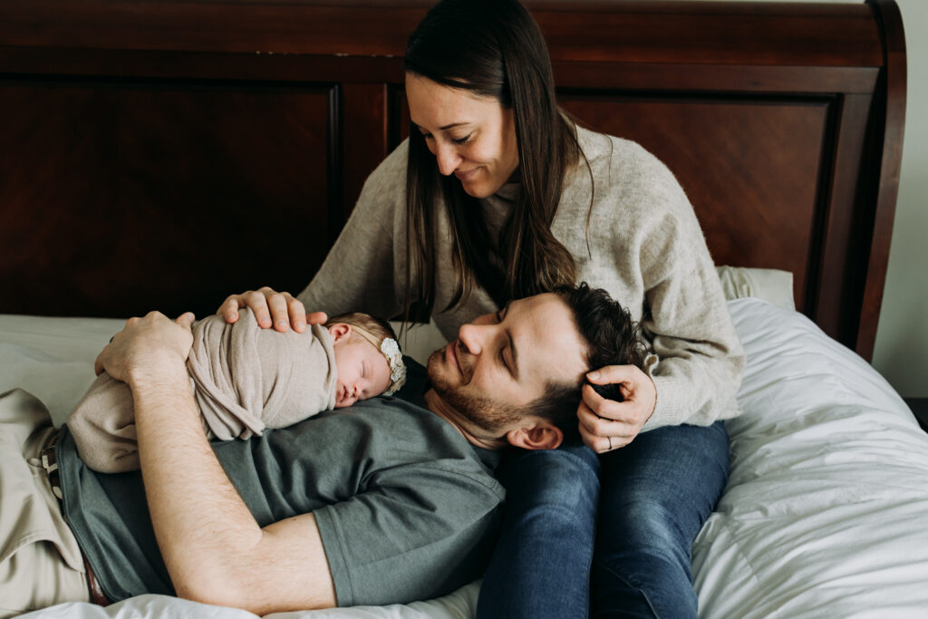 parents cuddling on bed with their baby for newborn photo session in Pittsburgh PA