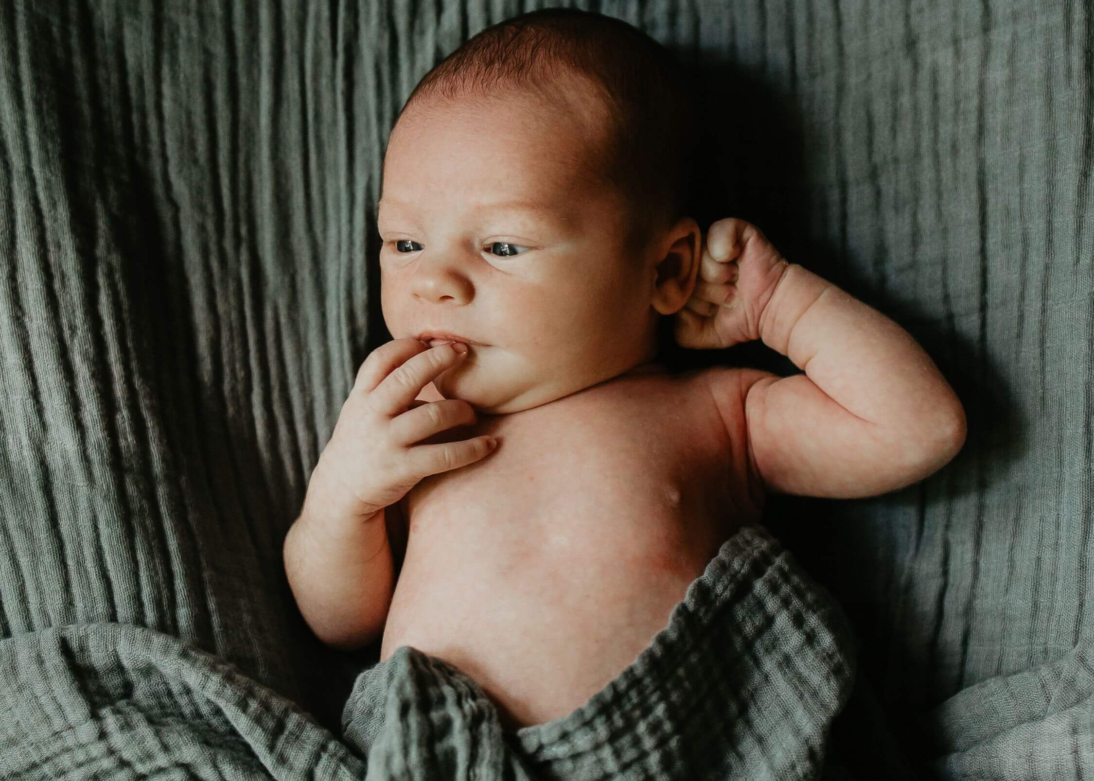 A newborn baby lays on a green blanket with eyes open thanks to lactation consultant pittsburgh