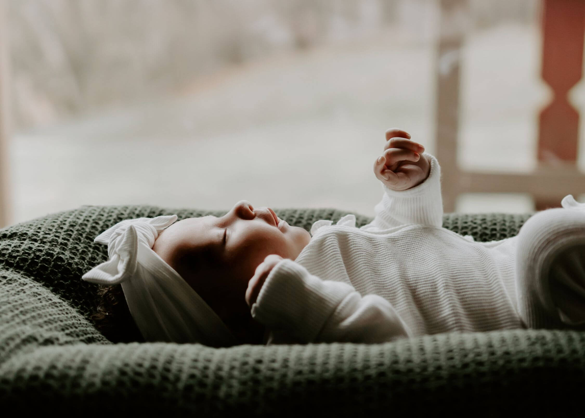 A newborn baby sleeps in a pad in a white onesie and bow